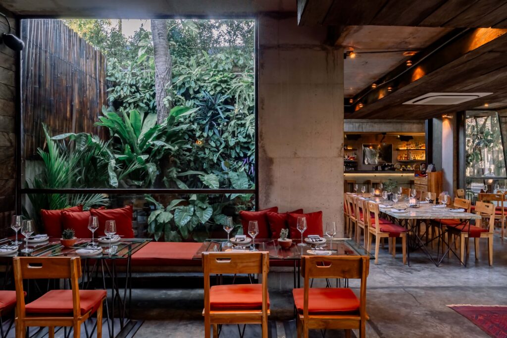 Restaurant dining area with tables set for meals, overlooking a lush green garden through a large window