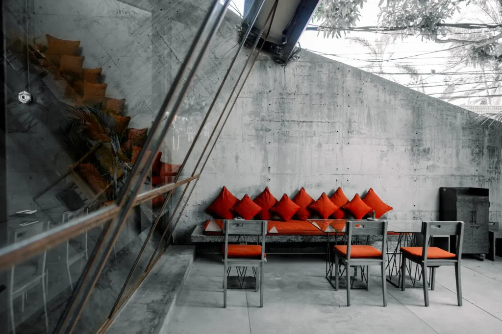 A modern indoor seating area with concrete walls, red cushioned benches, and matching red pillow backs.