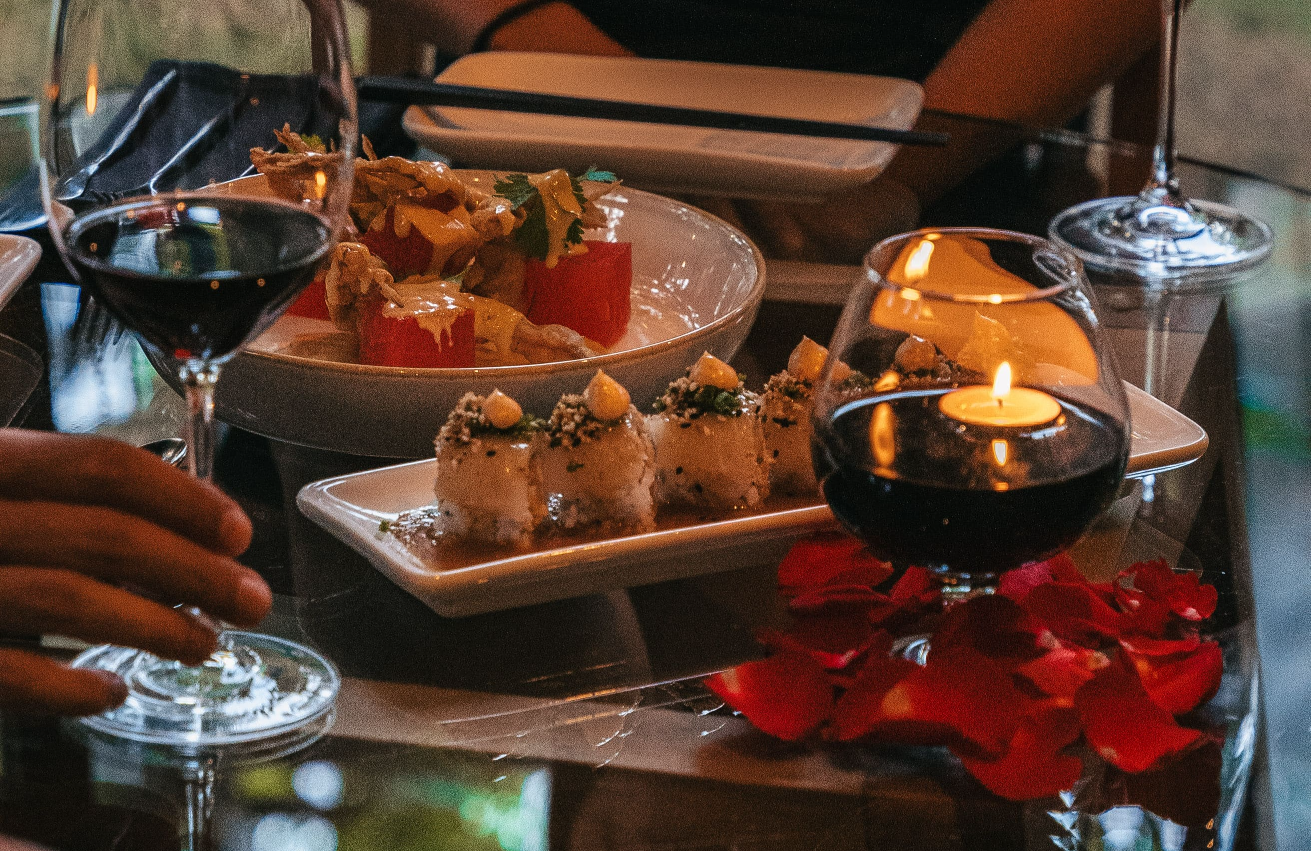 A round glass table set for a meal, featuring plates of sushi rolls and a dish garnished with greenery.