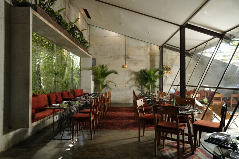 A modern restaurant featuring a large glass wall and an expansive dining table, inviting a bright and open atmosphere.