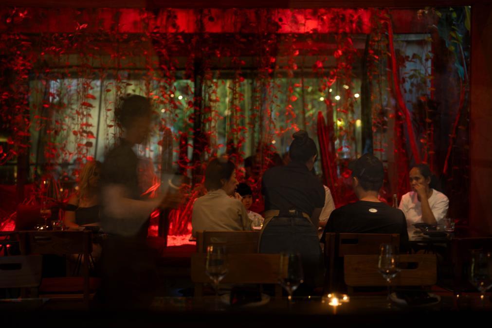 Diners seated at tables in a restaurant illuminated by soft red lighting, creating a warm and inviting atmosphere.