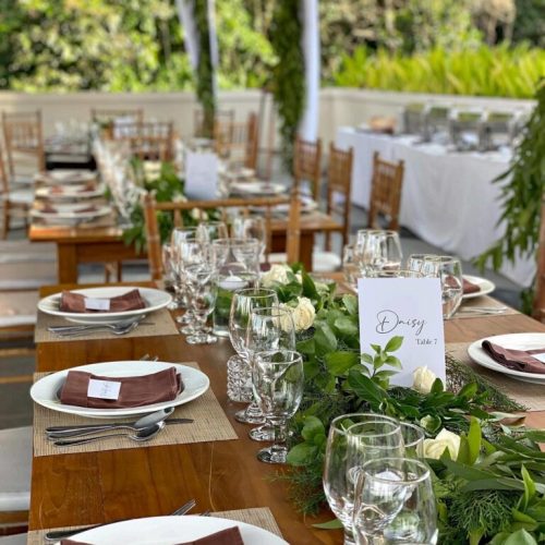 Outdoor dining setup with long tables and greenery decorations."
