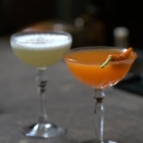 Two signature cocktails served in stemmed coupe glasses on a wooden bar top at Kilo Seminyak