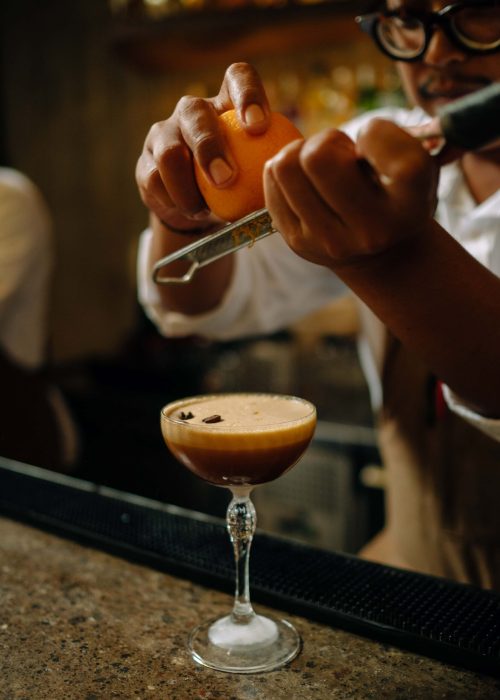 Bartender grating fresh lemon zest over a cocktail for garnish